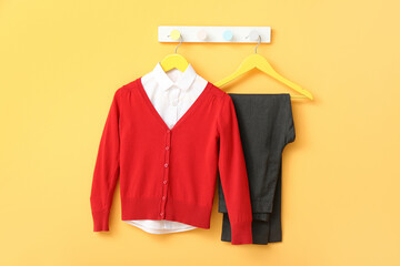 Stylish school uniform hanging on rack against yellow wall