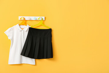 Stylish school uniform hanging on rack against yellow wall
