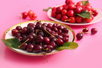 Plates with sweet cherries and leaves on pink background