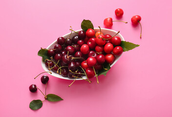 Bowl with sweet cherries and leaves on pink background
