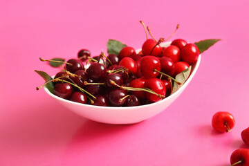 Bowl with sweet cherries and leaves on pink background