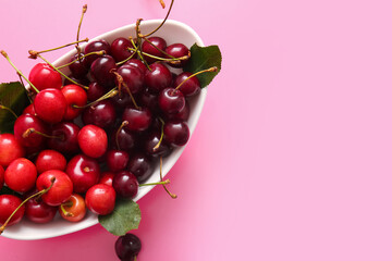 Bowl with sweet cherries and leaves on pink background