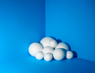 Multiple different sized white textured spheres in the corner of bright blue walls and floor. Minimalism. Design concept