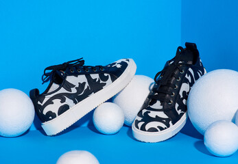 Close up view of trendy white textile sneakers with black plant motifs. White rubber sole and black...