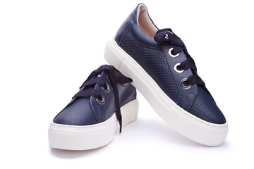 A close up view of modern female navy blue leather sneakers isolated on the white background. Design with perforation, thick shoelaces and metal eyelets, white sole. Urban style concept.