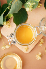 Wooden board with jar of linden honey on brown background