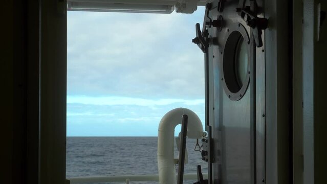 Ship is rocking on swell. Pitching. Iron door with porthole si open. After the storm