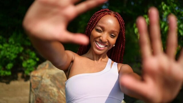 Outdoor portrait natural Beautiful young African American woman red braids hair style, perfect white teeth smile, laughing closing camera with hands at sunny summer day with green foliage background