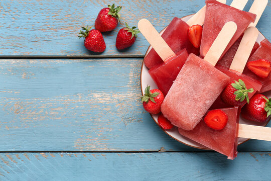 Plate with sweet strawberry ice-cream popsicles on blue wooden background