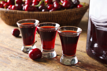 Shots of sweet cherry liqueur and wicker bowl with fresh berries on wooden background