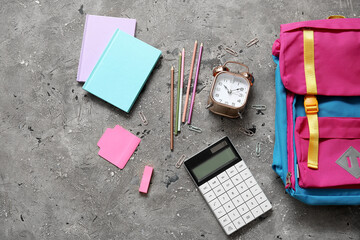 Colorful school backpack with notebooks, alarm clock and calculator on grey grunge background
