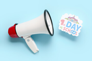 Megaphone and sheet with text 1ST DAY OF SCHOOL on blue background