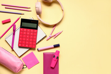 Modern calculator with headphones and different stationery on pale yellow background