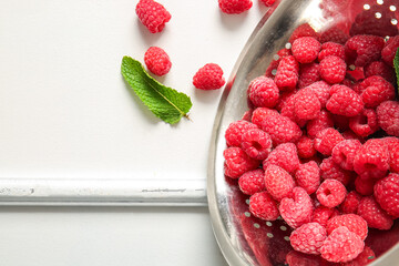 Colander with fresh raspberries and mint on white background