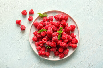 Plate with fresh raspberries and mint on light blue background