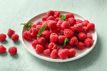 Plate with fresh raspberries and mint on light blue background