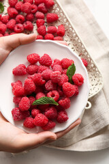 Female hands holding plate with fresh raspberries and mint, closeup