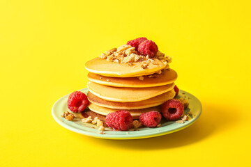 Plate of tasty pancakes with raspberries on yellow background
