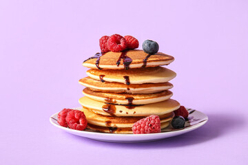 Plate of tasty pancakes with raspberries and blueberries on lilac background