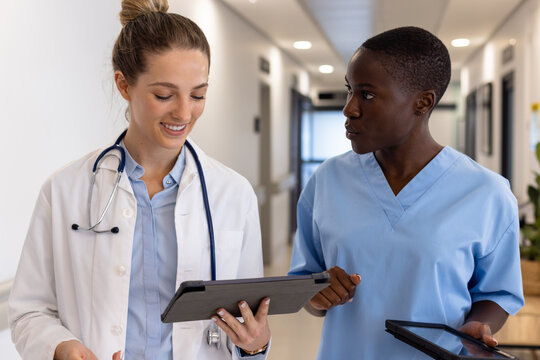 Diverse female doctors using tablets and talking in corridor at hospital