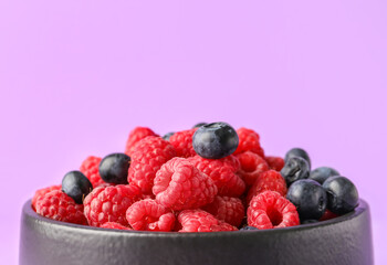 Bowl with fresh raspberries and blueberries on lilac background