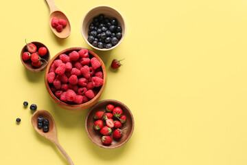 Bowls with fresh raspberries, blueberries and strawberries on yellow background
