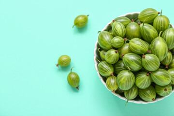 Bowl with fresh green gooseberry on turquoise background, closeup