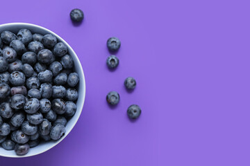 Bowl with fresh blueberry on purple background, closeup