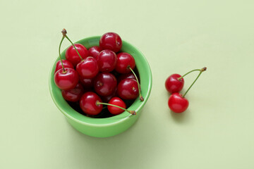 Bowl with fresh cherry on green background, closeup