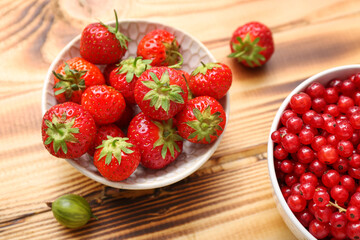 Bowls with fresh strawberry and red currant on wooden background, closeup