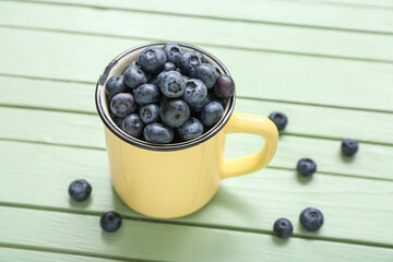 Cup with fresh blueberry on color wooden background, closeup