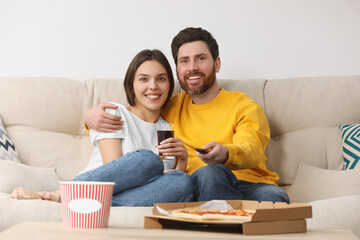 Fototapeta premium Happy couple watching TV with popcorn and pizza on sofa
