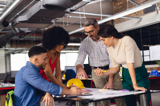 Diverse business people looking at architectural plans and discussing work at office