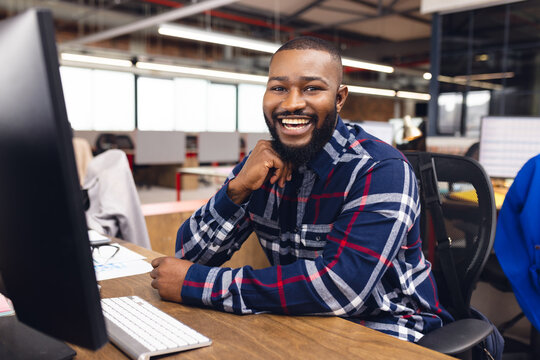 Portrait of happy african american businessman using computer and smiling at office