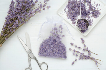 Scented sachet with dried lavender flowers and scissors on white wooden table, flat lay