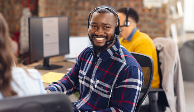 Portrait of happy african american businessman using phone headset and smiling at office