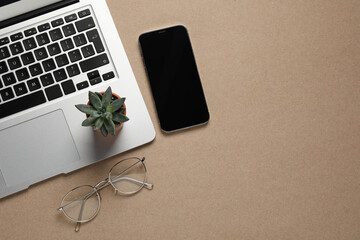 Modern laptop, houseplant, glasses and smartphone on beige table, flat lay. Space for text