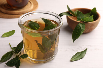 Cup of freshly brewed tea with bay leaves on white wooden table, closeup