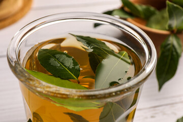 Cup of freshly brewed tea with bay leaves on white wooden table, closeup
