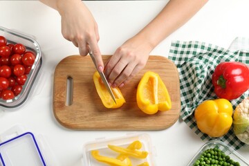Woman cutting bell pepper and containers with fresh products on white table, flat lay. Food storage