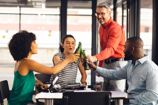 Happy diverse casual business colleagues making a toast with bottles of beer in office