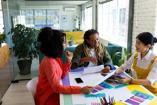 Happy diverse male and female creatives sitting at table discussing project in design meeting