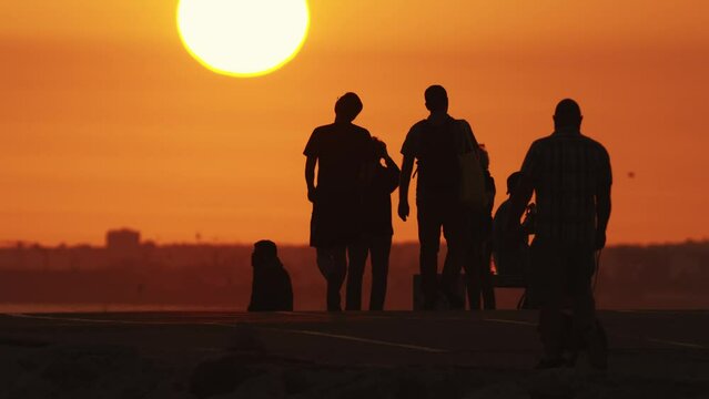 Black silhouettes of people spending time on the hill and walking out their pets at sunset