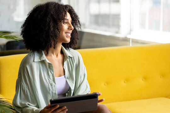 Happy biracial casual businesswoman using tablet sitting on sofa in office, copy space