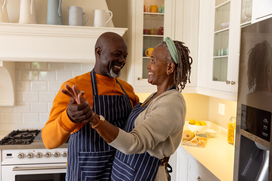 Happy african american senior wearing aprons having fun dancing together in kitchen