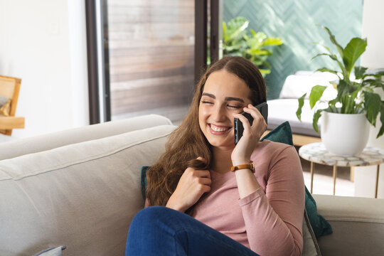 Happy caucasian woman on couch talking on smartphone at home