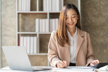 Beautiful asian businesswoman working with laptop and financial documents on desk, company employee holding accounting documents Checking financial data or market reports working in the office.