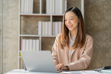 Beautiful asian businesswoman working with laptop and financial documents on desk, company employee holding accounting documents Checking financial data or market reports working in the office.