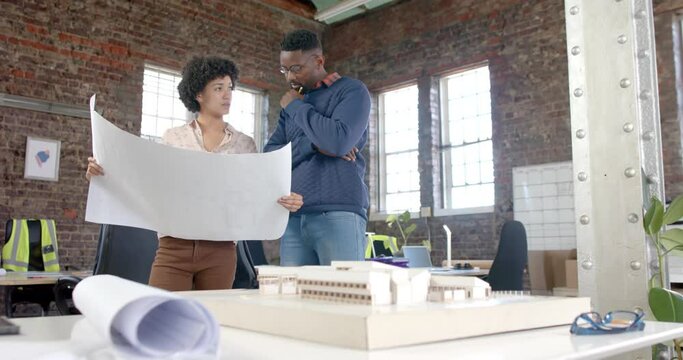 Diverse architect colleagues discussing work with building model and blueprints in slow motion