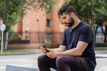 Fototapeta premium young man chatting with his cell phone in a park on the street of a city